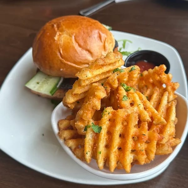 A Sugah Please burger with sliced cucumbers and waffle fries with a side of dipping sauce.
