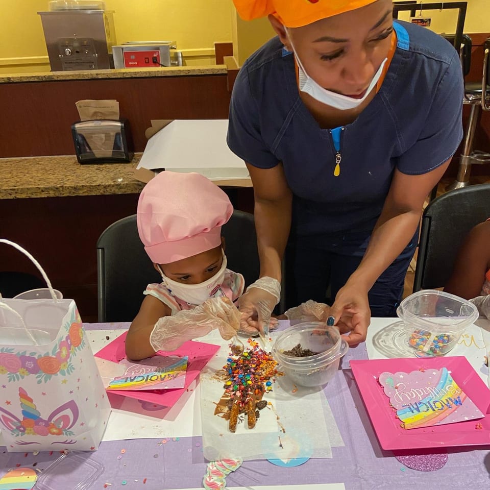 A child and adult decorating pretzels with colorful sprinkles and candies at Sugah Please.