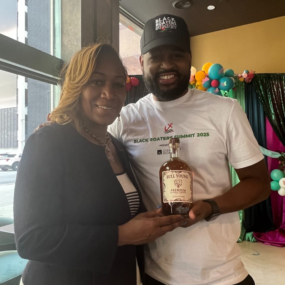Two people smiling, holding a bottle of Bull Young Premium Bourbon Whiskey at Sugah Please.