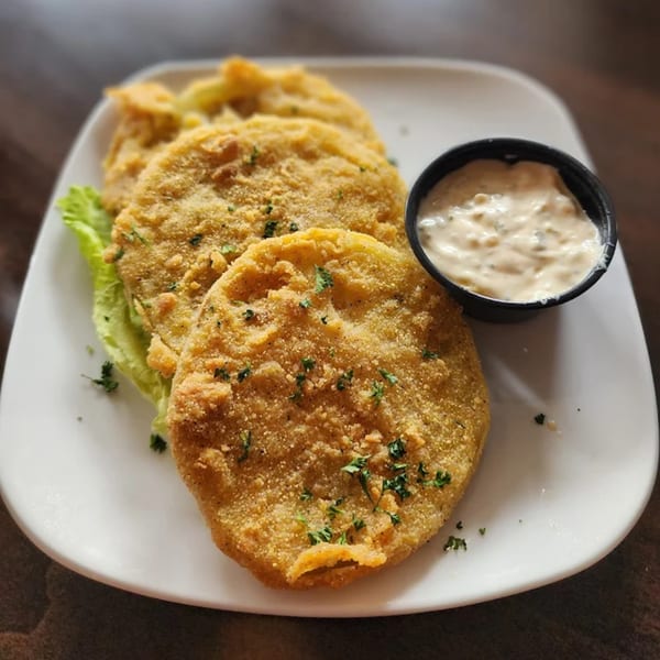 Golden-brown fried green tomatoes with fresh parsley and a side of creamy dipping sauce.