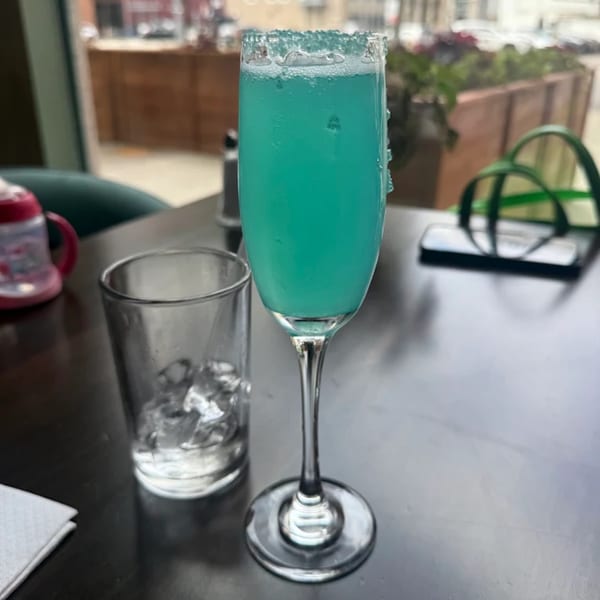 A blue mimosa with a sugared rim sits next to a glass of ice water on a dark table.