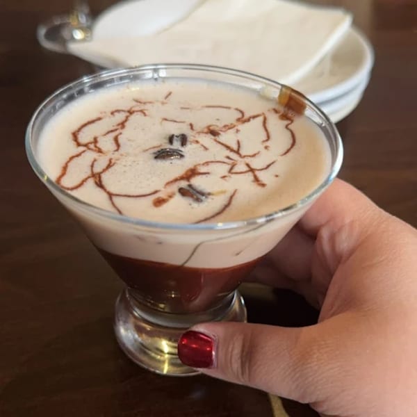 Hand holding a Sugah Please espresso martini with chocolate drizzle and coffee beans.