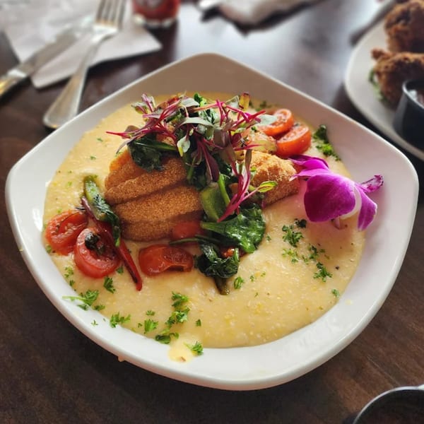 Sugah Please's shrimp and grits, garnished with microgreens, tomatoes, and an orchid.